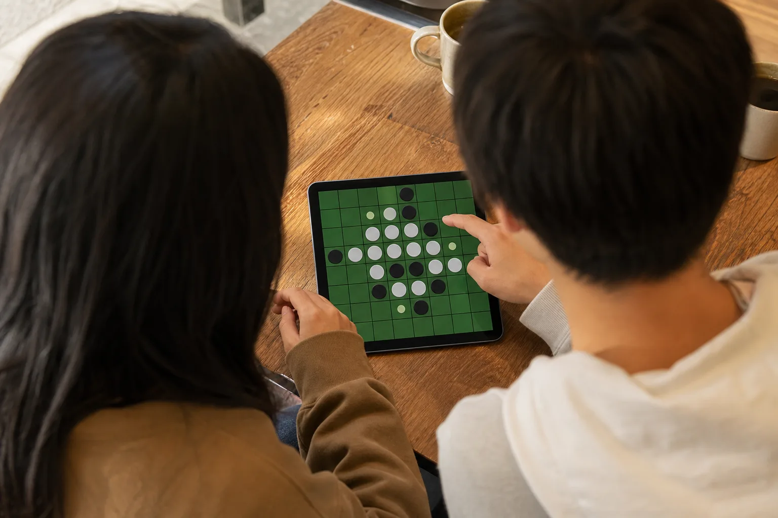 Two people sharing a tablet to play Reversi, seen from behind at the shoulders and hands